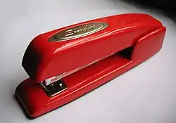 A small red stapler with the badge reading "Swingline" atop, seen from above on a white background with shadow at the top of the image