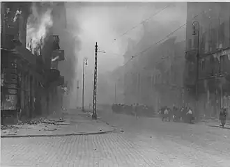 NARA copy #29, IPN copy #28 Transporting of Jews onward Column heading North to Umschlagplatz on Zamenhofa Street, with burning Zamenhofa 25 / Wołyńska 2 on the left.