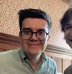 close-up image of Stuart Ritchie wearing a pastel green shirt, grinning at camera