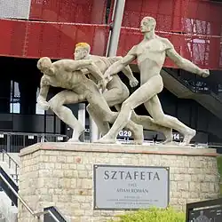 Sculpture of three nude runners, two passing a baton