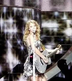 Swift singing on an acoustic guitar wearing a sparkly dress