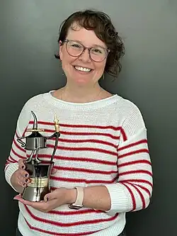 Half-length portrait of Telgemeier, holding an Inkpot Award, wearing a white shirt with red stripes, and smiling