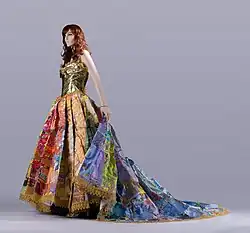 A mannequin wears a multicolored gown with a golden bodice, full skirt, and flowing train.