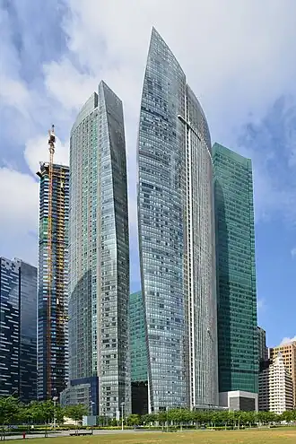 Ground-level view of two curved buildings that slightly resemble sails; the sun is setting in the distance.