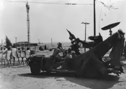 A group of people clad in white march through a desert landscape with a bizarre vehicle