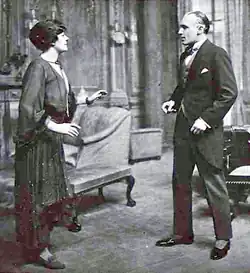 stage scene depicting a youngish white woman and a youngish, clean-shaven white man in morning dress looking at each other