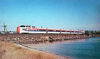 A white passenger trainset with red and blue horizontal stripes on the side and red noses on both ends