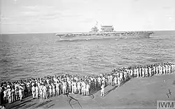 Black and white photo of men standing on the deck of a ship looking at another ship which is sailing nearby