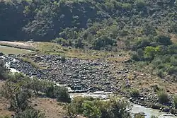 A boulder-strewn ford across a river, the approaches to which are sloped and vegetated