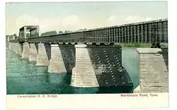 A photograph of a railroad bridge crossing a river; the piers are made of stone, while the deck is made of iron.