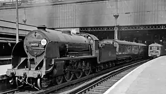 A steam locomotive waiting with its train at a station