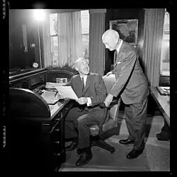 William Kaufman seated in a desk chair smiling back at father Alvin who is standing behind him smiling in return.