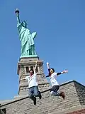 Two participants of the Work and Travel program jump in front of the Statue of Liberty