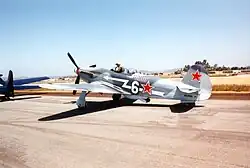 Propeller fighter on tarmac with pilot standing up in open cockpit. Red star