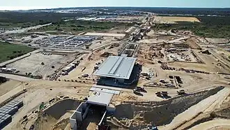 Drone shot of a sandy construction site. The station now has its roof constructed.